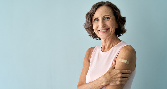 Older woman smiling with holding arm with small upper arm bandaid